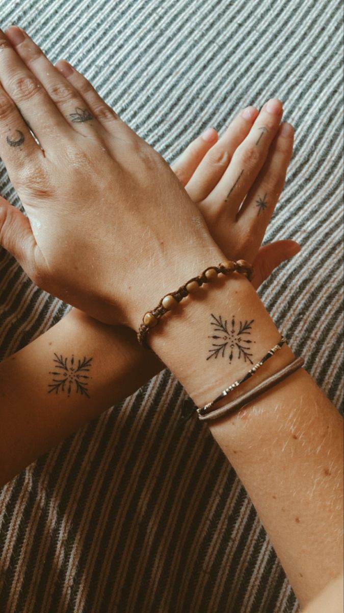 two women with matching tattoos on their arms holding hands up to each other, both wearing bracelets