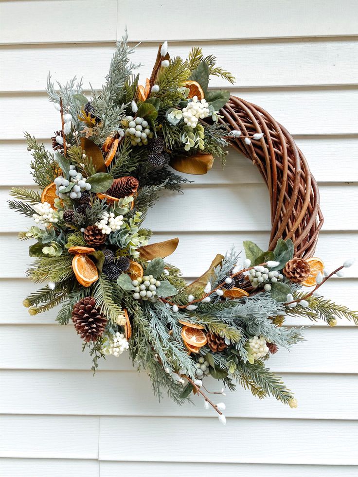 a wreath is hanging on the side of a white house with pine cones and evergreens