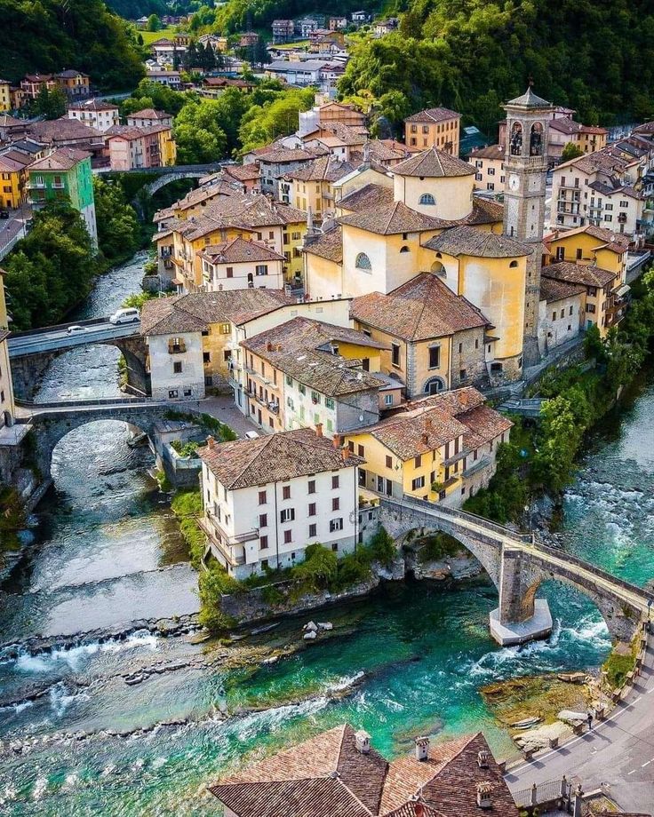 an aerial view of a river running through a town with buildings on the bank and bridge over it