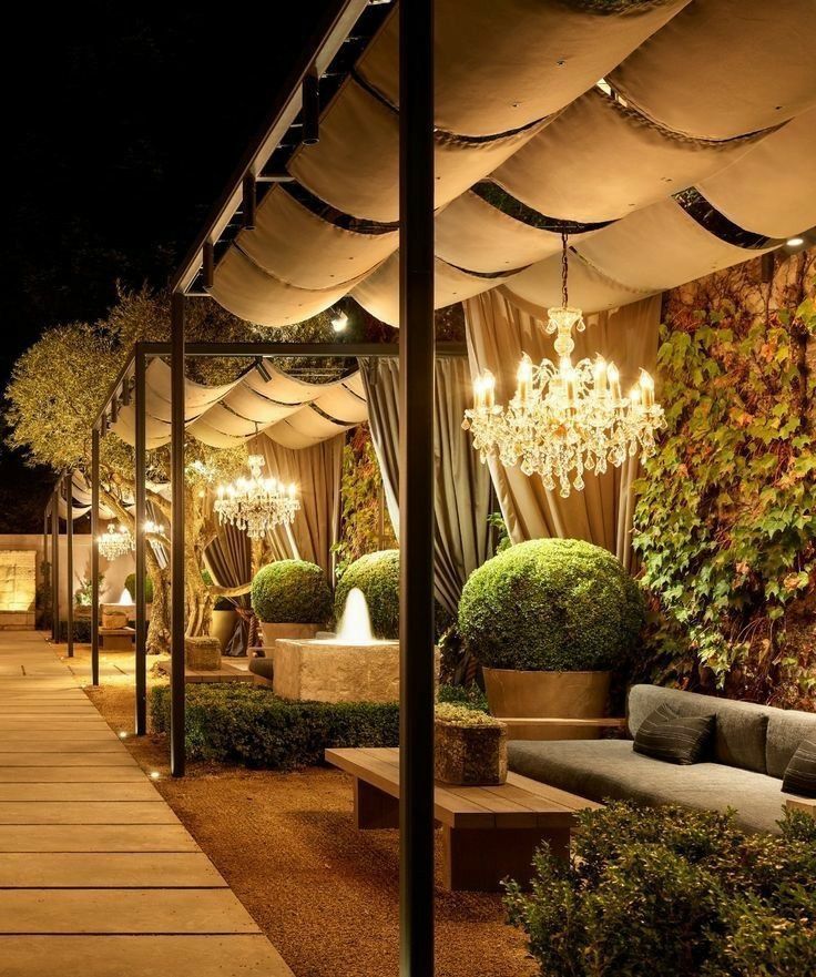 an outdoor seating area is lit up with chandeliers and greenery at night