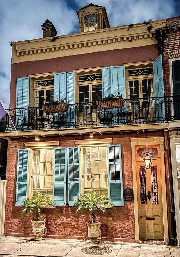 an old building with blue shutters and potted plants on the front porch is shown