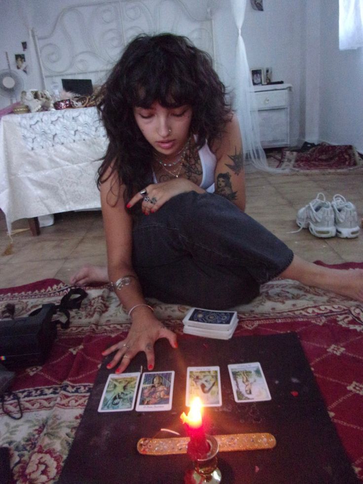 a woman sitting on the floor next to a table with cards and a lit candle