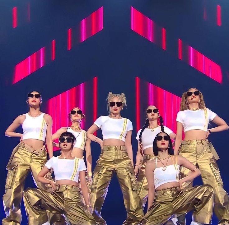 a group of women standing on top of a stage wearing gold pants and white shirts