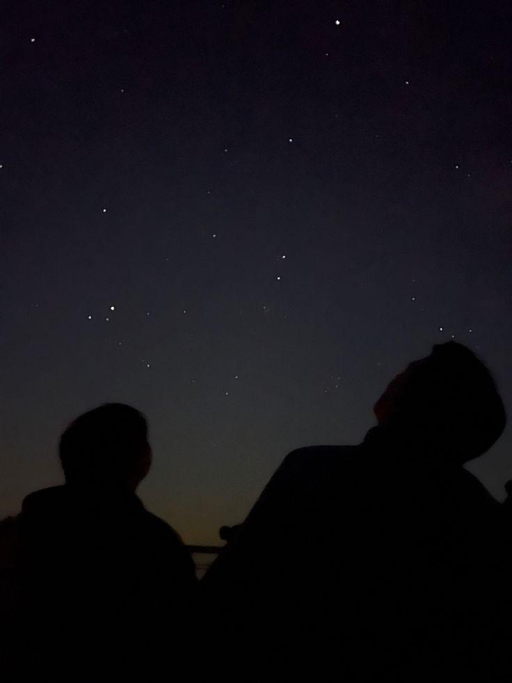 two people looking up at the night sky with stars in the distance and one person sitting down