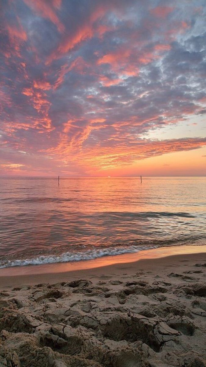 the sun is setting over the ocean with rocks on the shore and water in the foreground