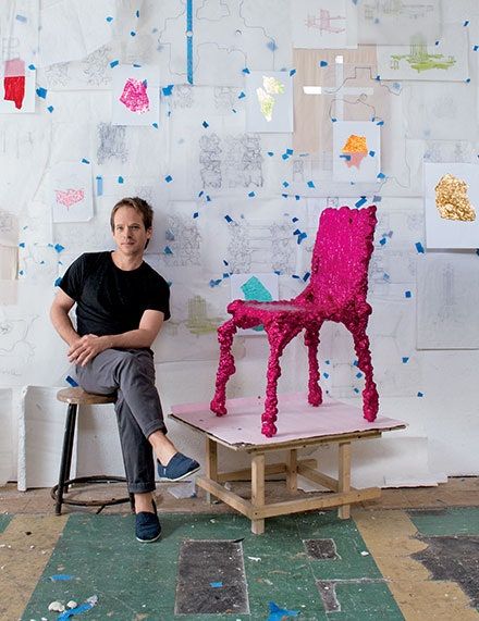 a man sitting in front of a chair made out of paper mache and yarn