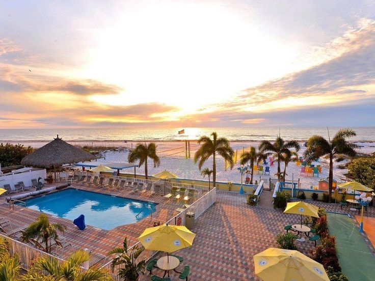 an outdoor swimming pool with umbrellas and tables next to the ocean at sunset or sunrise