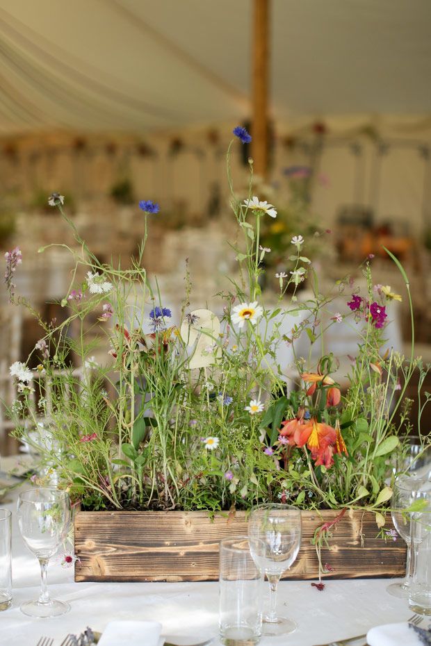 a wooden box filled with lots of flowers on top of a table covered in white linens