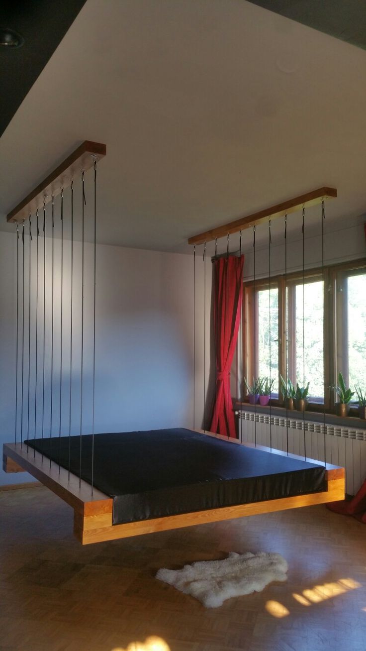 a bedroom with a bed suspended from the ceiling and hanging curtains on the windowsill