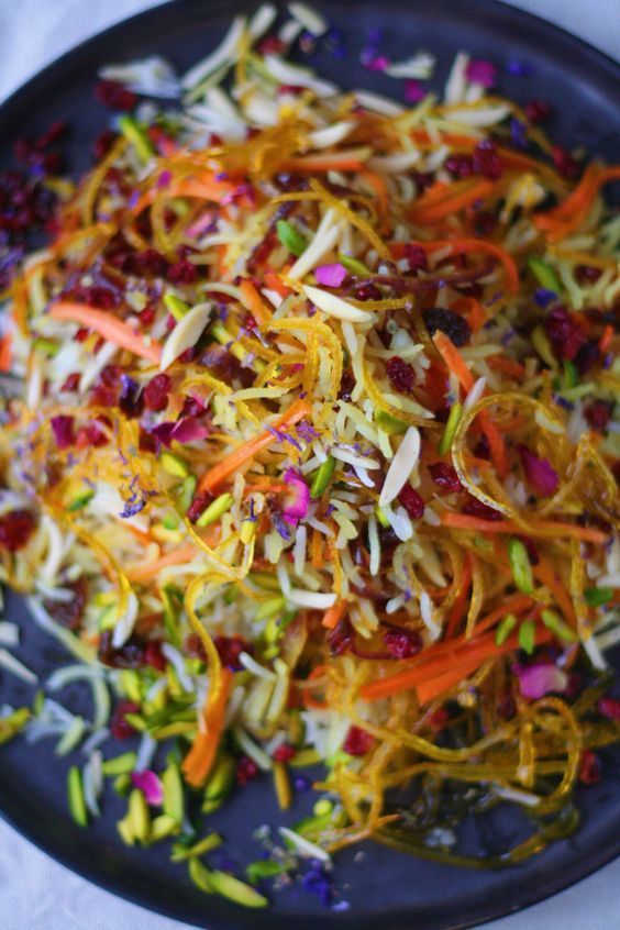 shredded carrots and cranberries on a black plate with white table cloth in the background