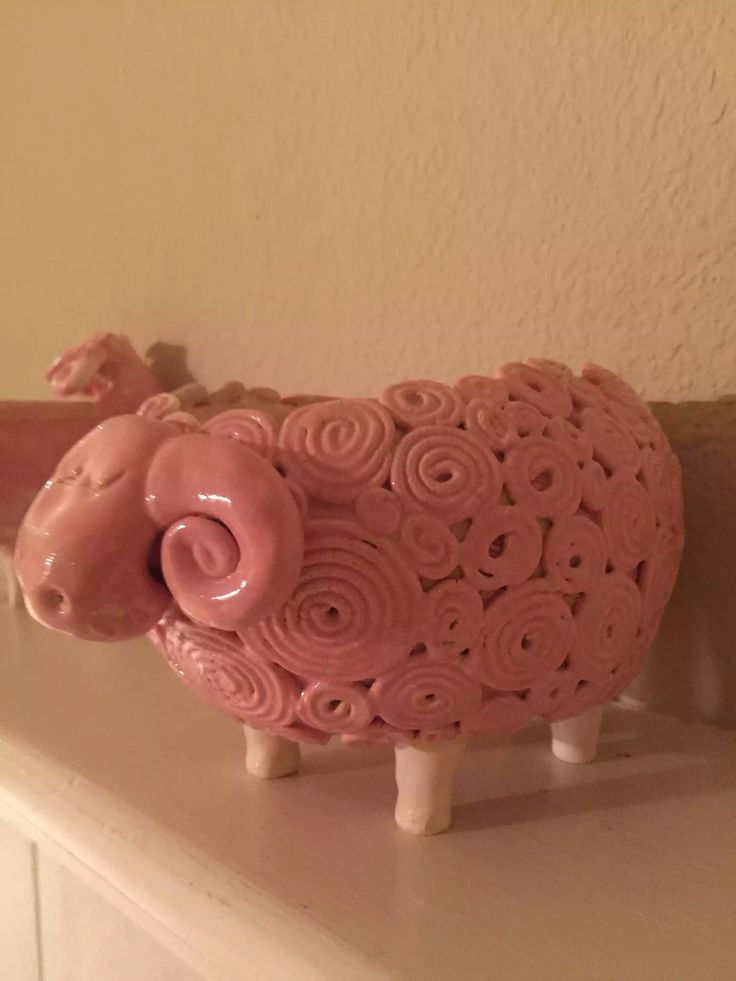 a pink sheep figurine sitting on top of a white shelf next to a wall