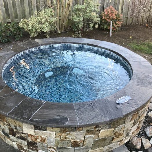 an outdoor hot tub in the middle of a yard with rocks and gravel around it