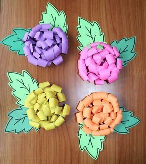 four different colored paper flowers sitting on top of a wooden table