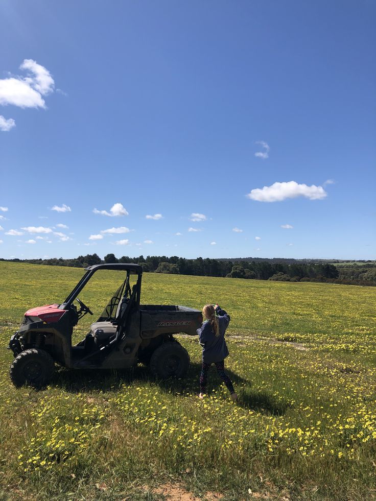 a woman standing next to a small child near a vehicle in a field with yellow flowers