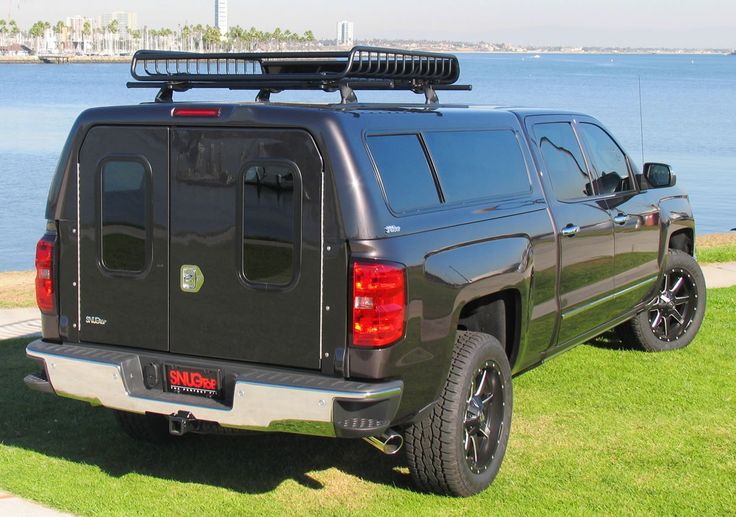 a black truck parked on top of a lush green field next to the ocean in front of a large body of water