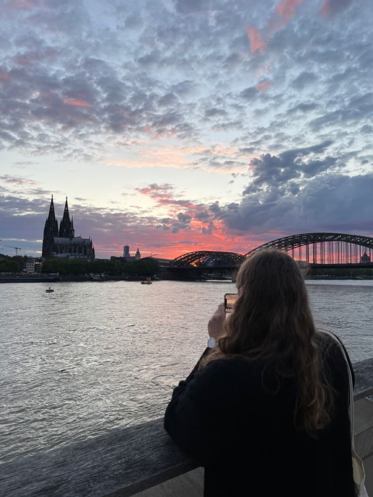 a woman is looking out over the water with a bridge in the background at sunset