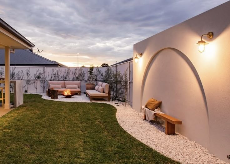 an outdoor living area is lit up at night with lights on the wall and furniture in the yard