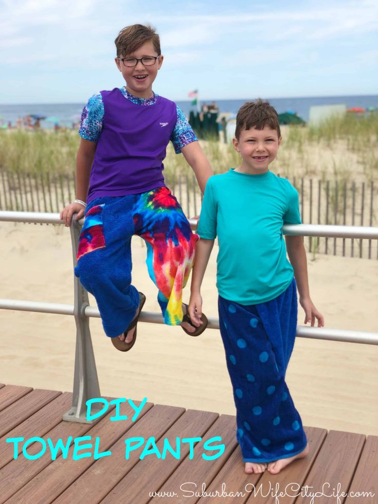 two young boys are standing on a railing by the beach