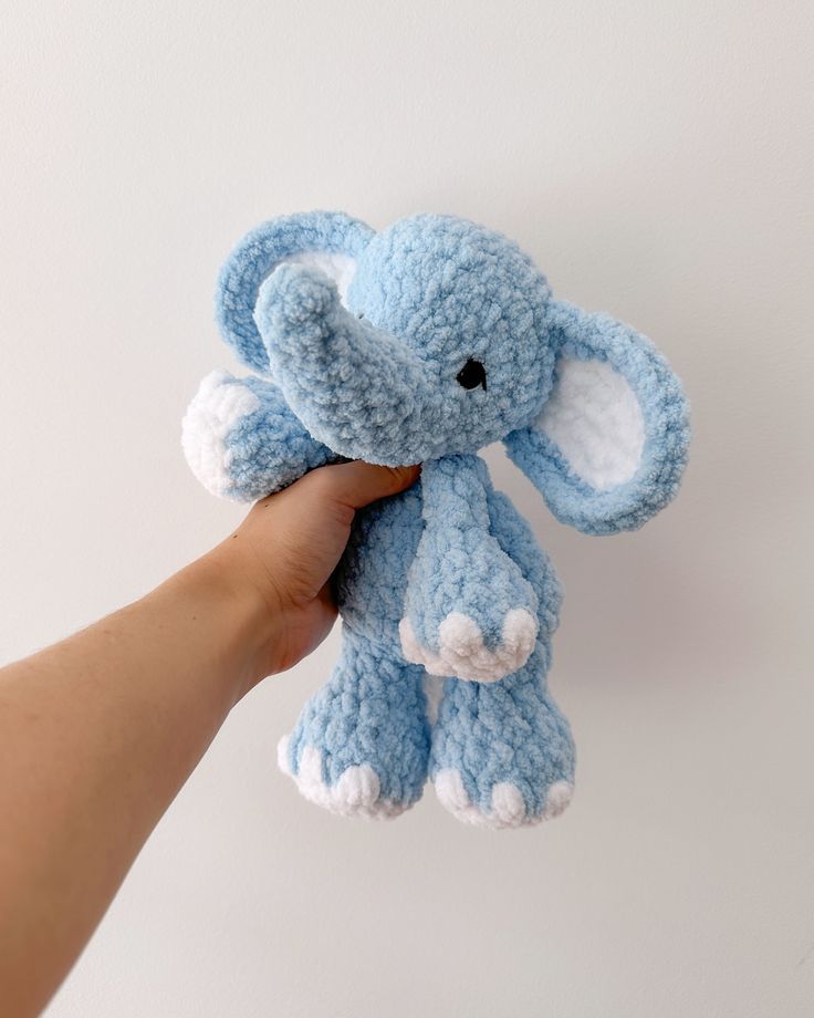 a small blue crocheted elephant is held by a person's hand against a white wall