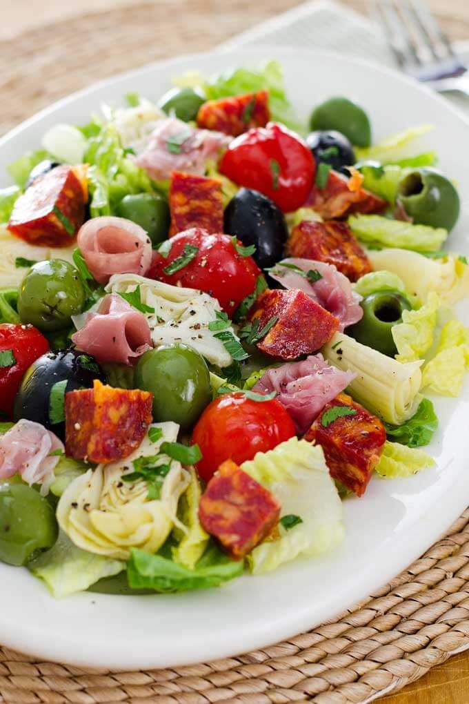 a white plate topped with salad and olives on top of a woven place mat