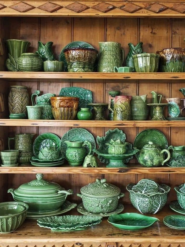 a shelf filled with lots of green dishes and vases on top of wooden shelves