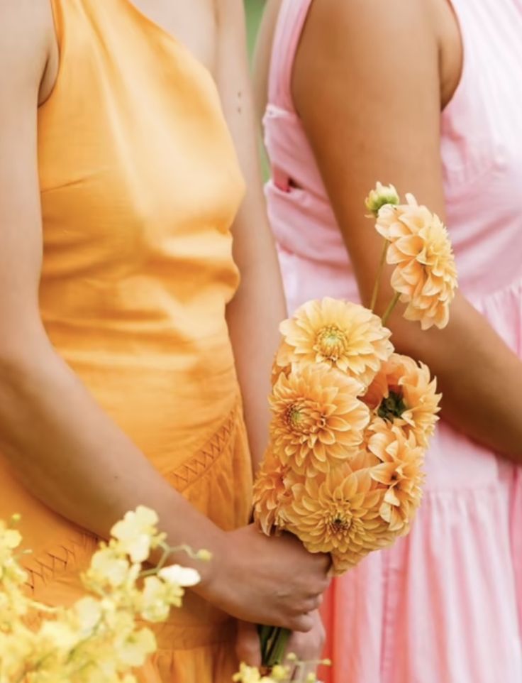 two bridesmaids holding bouquets of yellow and orange flowers in their hands,