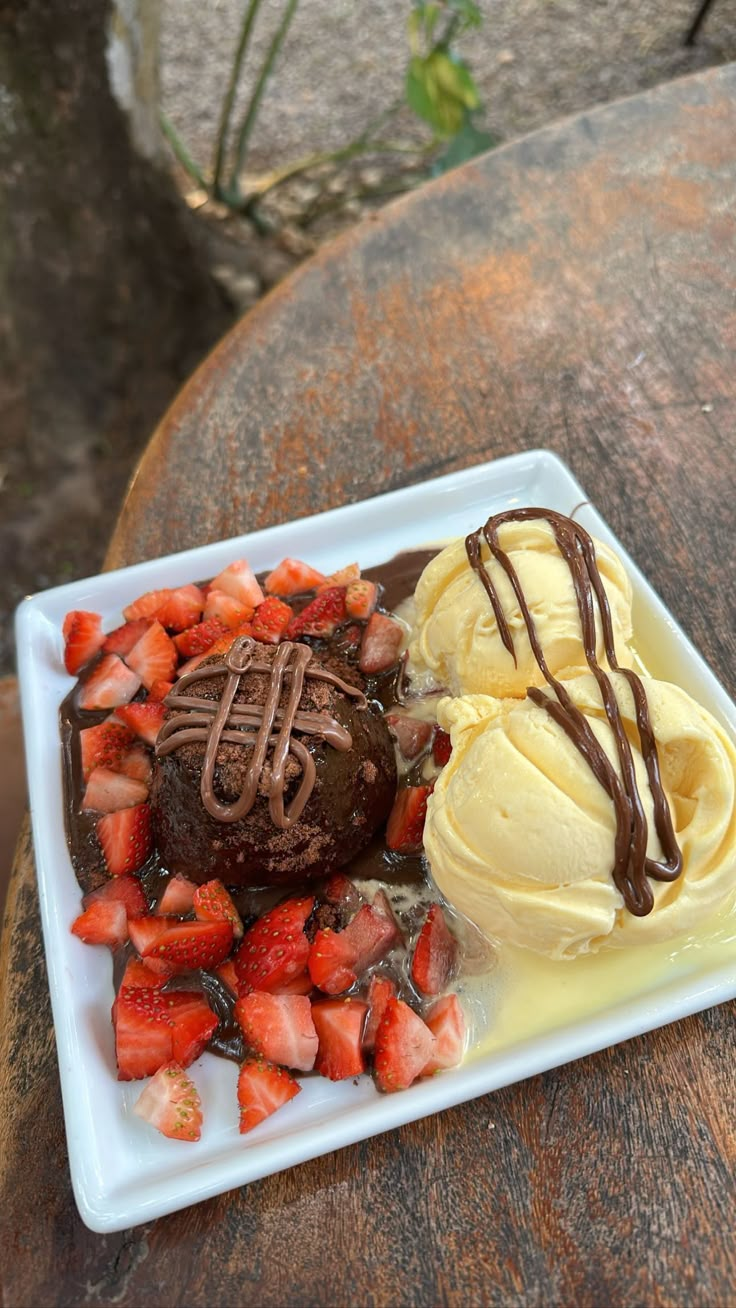 two desserts on a plate with strawberries and ice cream sitting on a table