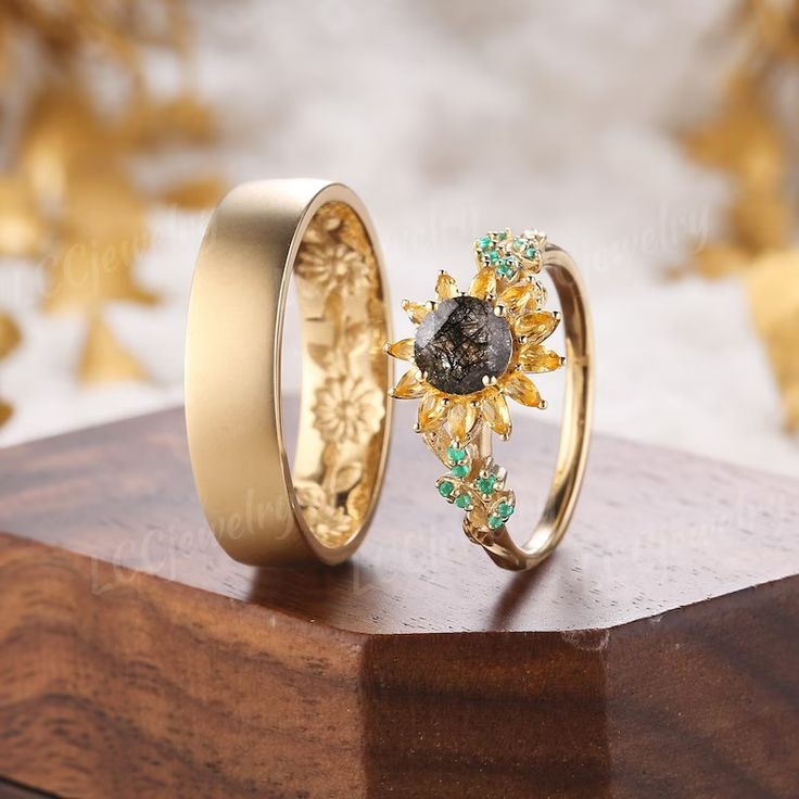 two wedding rings sitting on top of a wooden table next to gold and green flowers