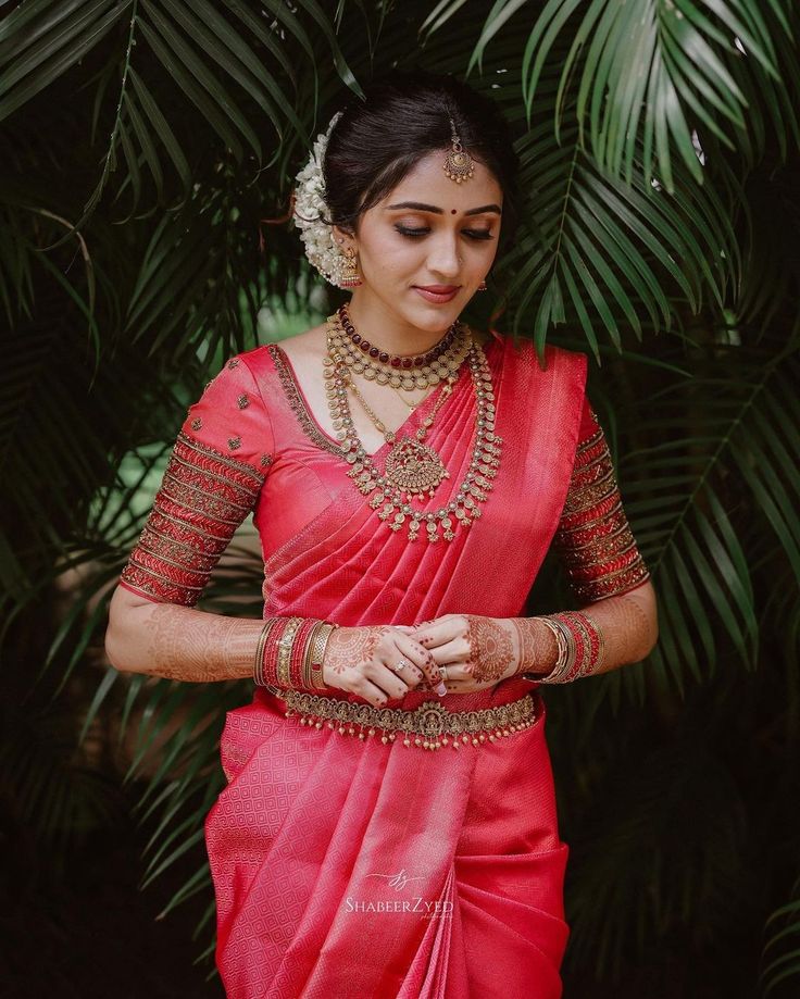 a woman in a red sari with jewelry on her hands and palm trees behind her