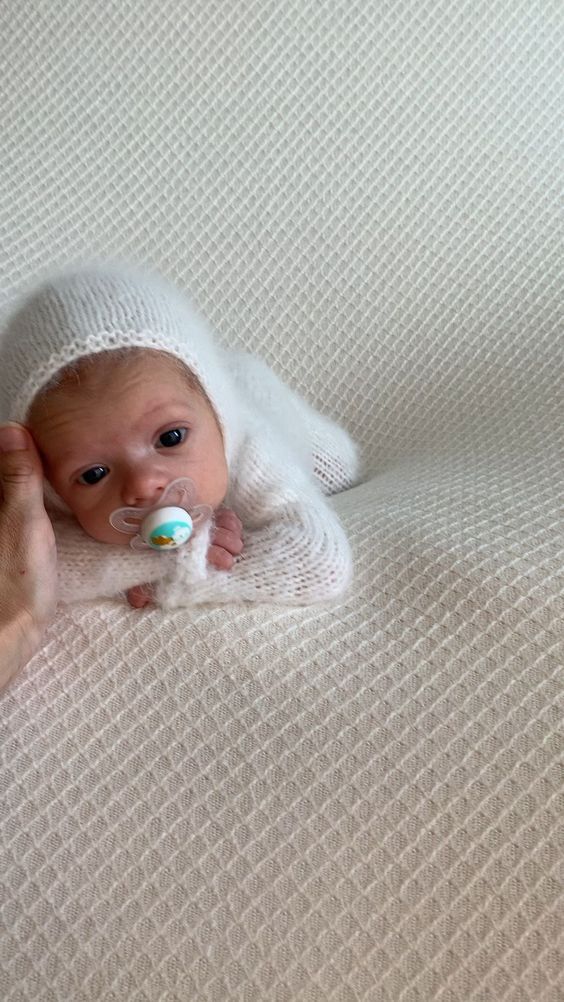 a baby laying on top of a white blanket with a pacifier in it's mouth