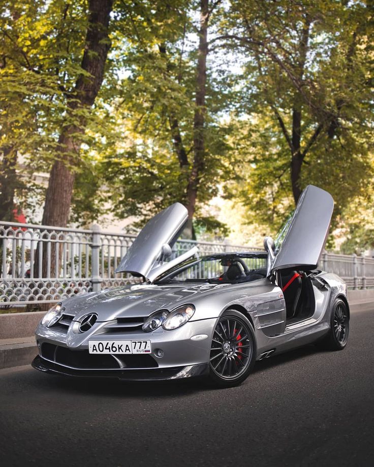 a silver sports car with its doors open on the road in front of some trees