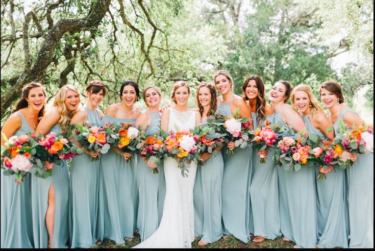 a group of women standing next to each other in front of trees and holding bouquets