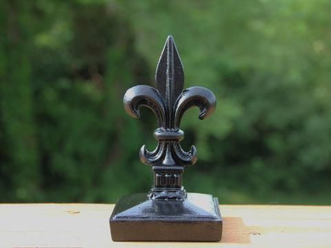 a metal fleur de lis on top of a wooden table with trees in the background