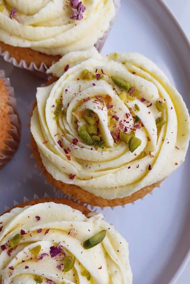 three cupcakes with white frosting and sprinkles on a plate