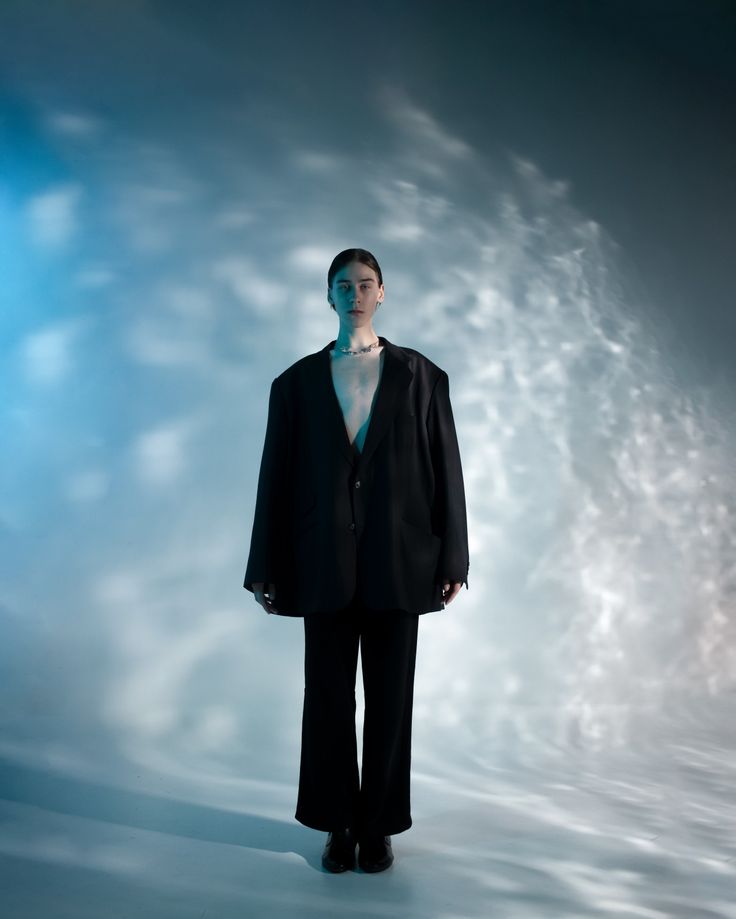 a woman standing in front of a blue background wearing a black suit and white shirt