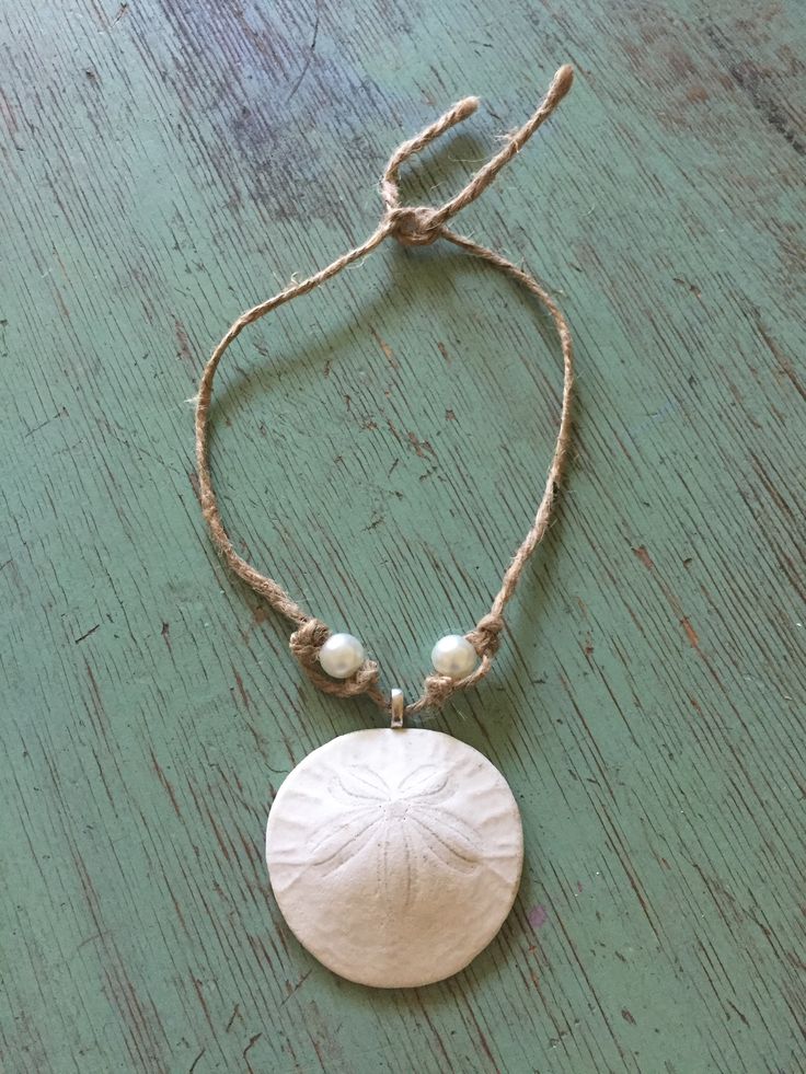 a white sand dollar on a string with a bead around it and a pendant