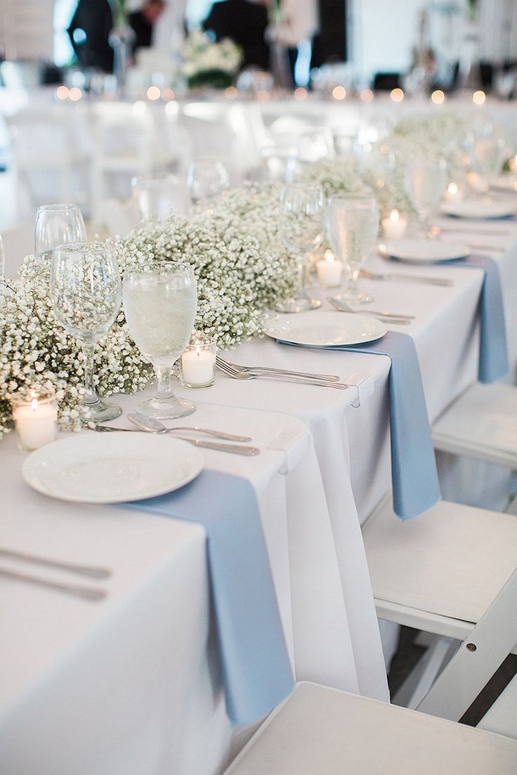 the table is set with white plates and silverware, baby's breath centerpieces