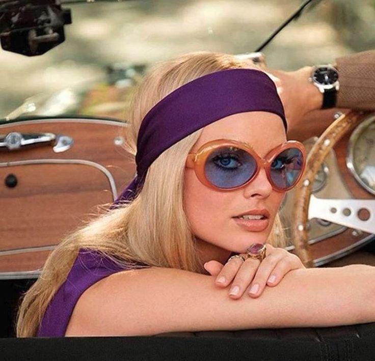 a woman in sunglasses and a headband leaning on the steering wheel of a car