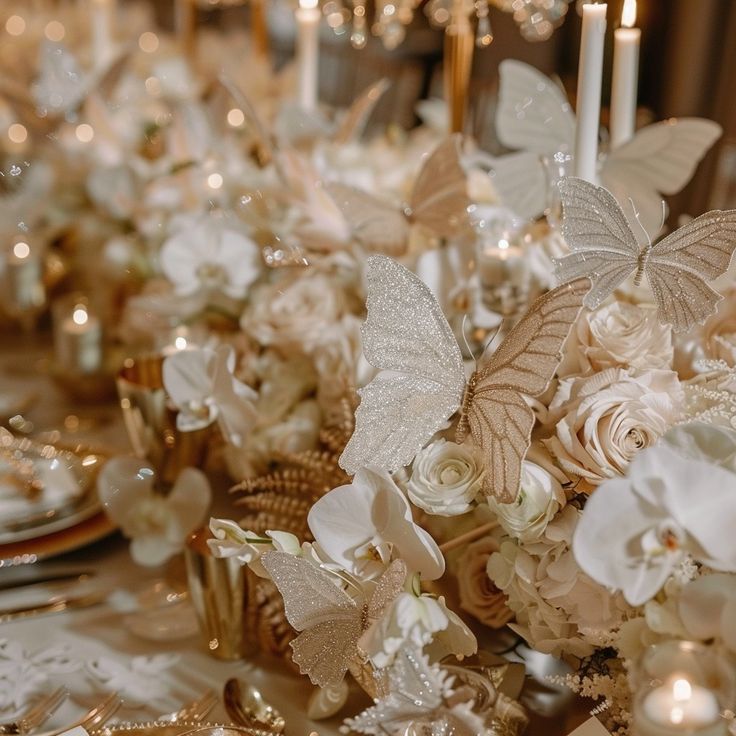 a table topped with lots of white flowers and gold plates covered in silver napkins