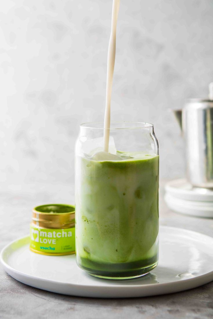 a glass filled with green liquid on top of a white plate next to a cup