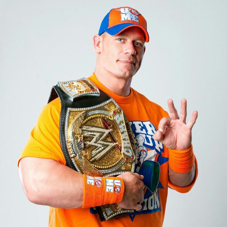 a man in an orange shirt and hat holding a wrestling belt