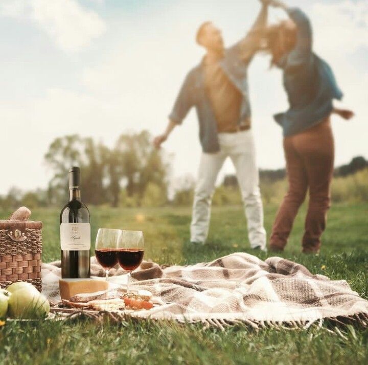 two people standing in the grass with food and wine