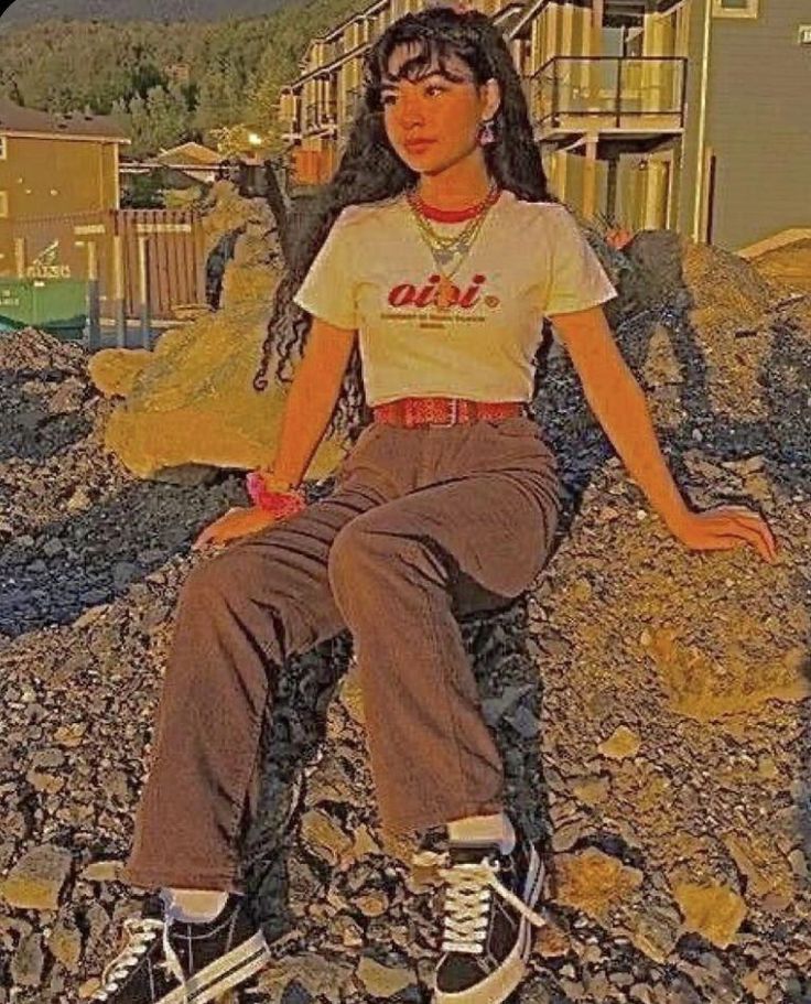 a woman sitting on top of a pile of rocks next to a house and mountains