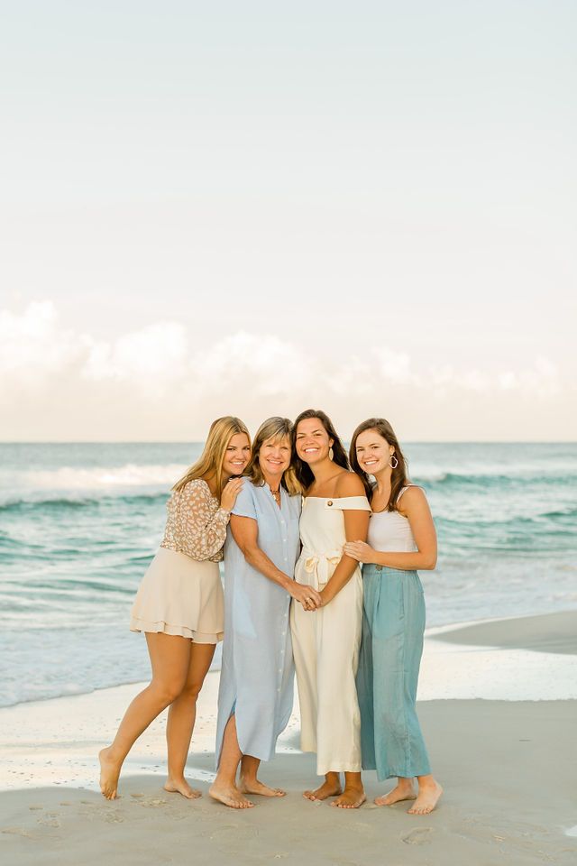 four women standing on the beach in front of the ocean with their arms around each other