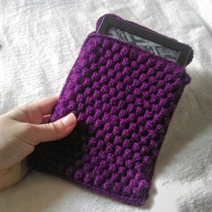 a hand holding an electronic device covered in purple crochet