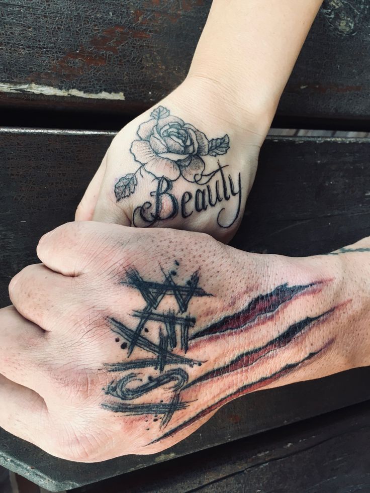 two hands holding each other with tattoos on their fingers and the words beauty written in black ink