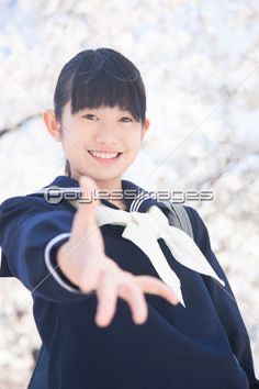 a young boy in blue jacket pointing at the camera with cherry blossom trees behind him