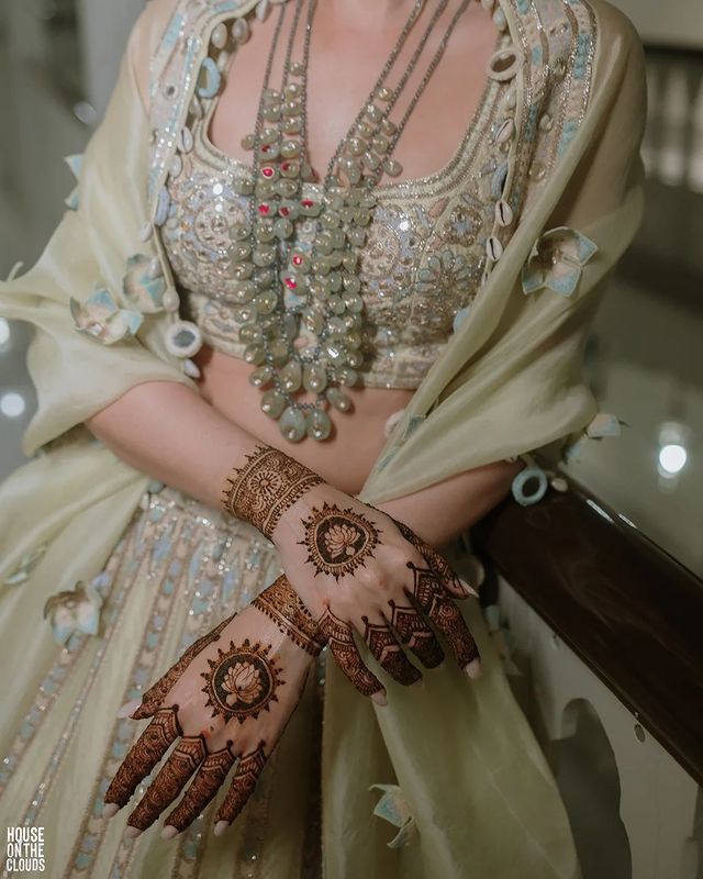 a woman in a bridal outfit with henna on her arm and hands, posing for the camera