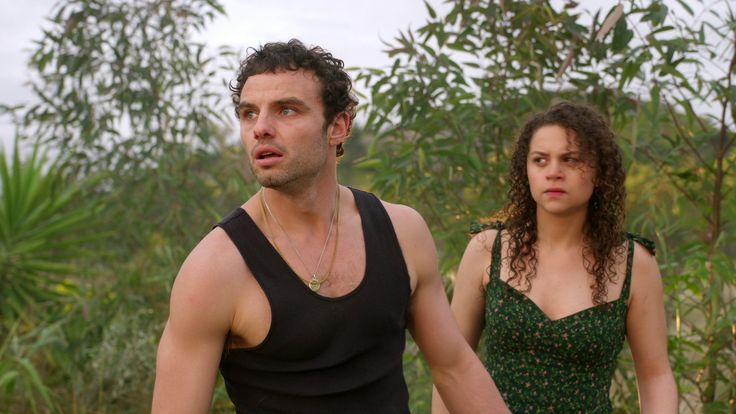 a man and woman standing next to each other in front of some trees with leaves