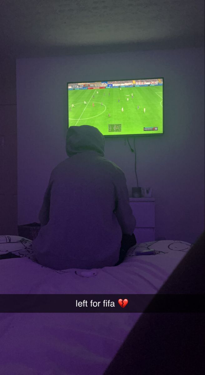 a person sitting on a bed in front of a flat screen tv that is turned on